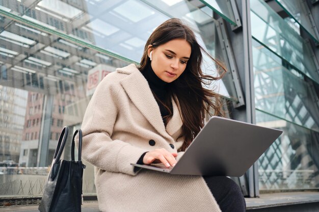 Young beautiful businesswoman confidently working on laptop on city street