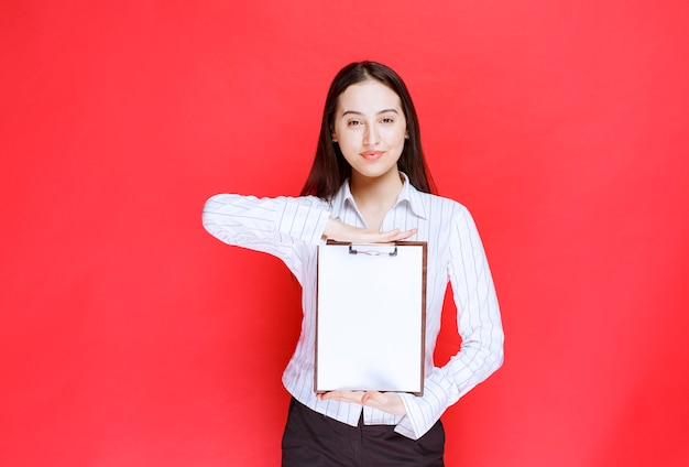 Free Photo young beautiful businesswoman holding empty clipboard over red wall. 