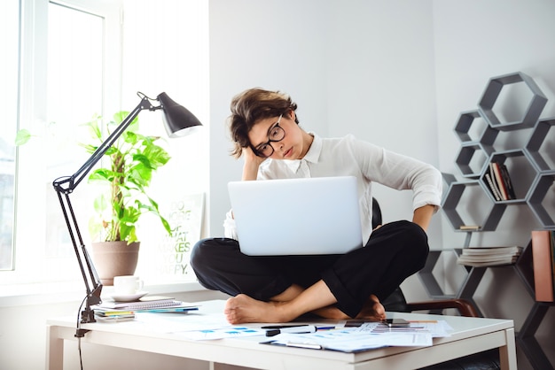 Young beautiful businesswoman sitting on table with laptop at workplace.