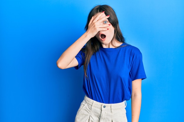 Young beautiful caucasian girl wearing casual clothes peeking in shock covering face and eyes with hand looking through fingers afraid