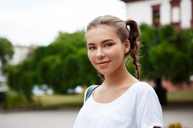 Young beautiful cheerful female student smiling, holding folders outdoors