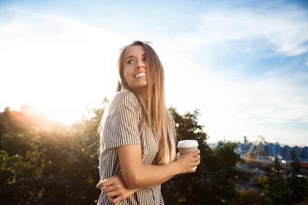 Free photo young beautiful cheerful woman walking around city, smiling, holding coffee.