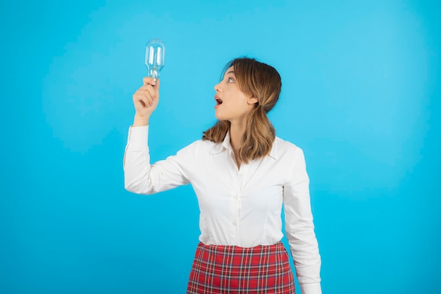 Young beautiful college girl holding idea bulb and looking at it with wide mouth. High quality photo