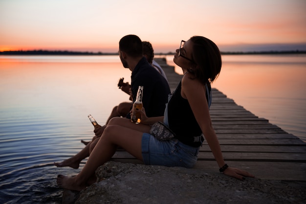 Free photo young beautiful company of friends resting at seaside during sunrise