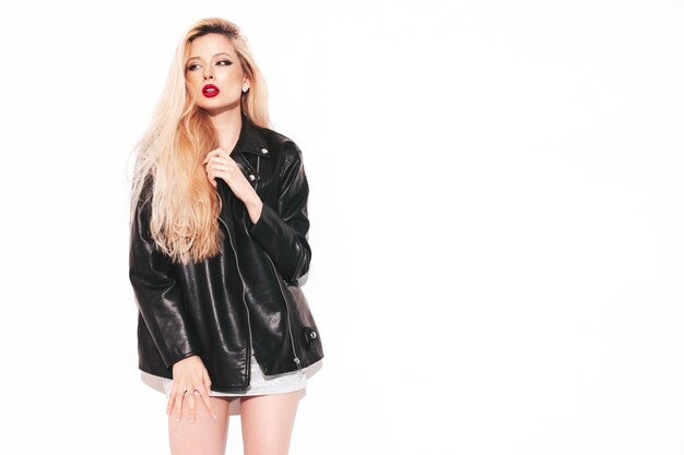 Young beautiful confident female in trendy summer evening silver dress Sexy carefree blond woman posing near white wall in studio Model in black leather biker jacket and red lips