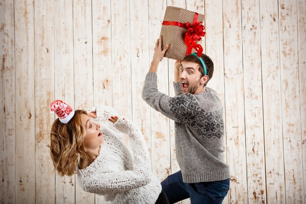 Young beautiful couple fighting for Christmas gift over wooden surface