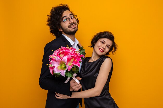 Young beautiful couple happy man with bouquet of flowers and woman smiling cheerfully embracing happy in love celebrating valentine