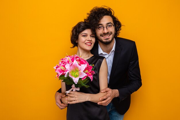 Young beautiful couple happy man and woman with bouquet of flowers smiling cheerfully embracing happy in love celebrating valentine