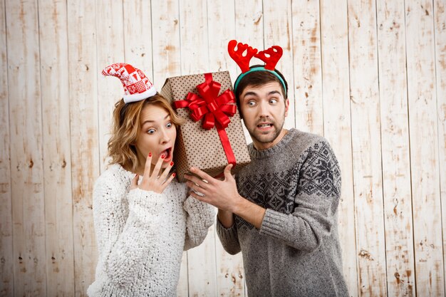 Young beautiful couple holding christmas gift over wooden wall