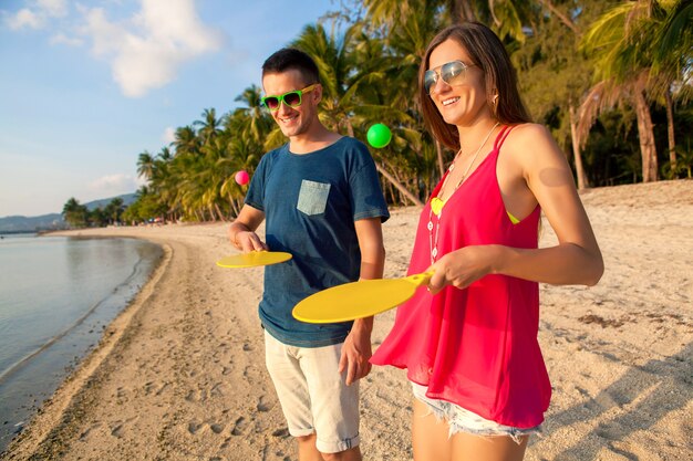 Young beautiful couple in love playing ping pong on tropical beach, having fun, summer vacation, active, smiling, funny, positive