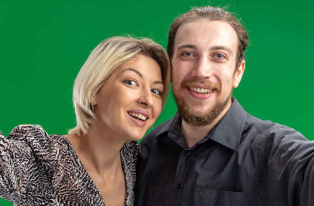 Free photo young beautiful couple man and woman looking at camera happy and cheerful smiling broadly celebrating valentines day standing over green wall