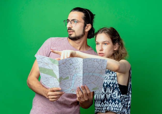 Free photo young beautiful couple man and women, confused man looking aside while his girlfriend pointing with finger at something over green background