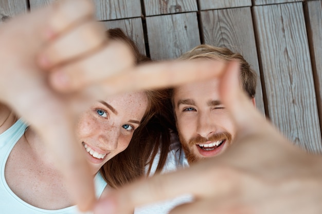 Free photo young beautiful couple smiling, lying on wooden boards making frame with hands focus at faces