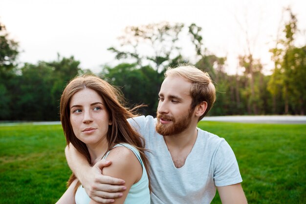 Young beautiful couple smiling, sitting on grass in park.