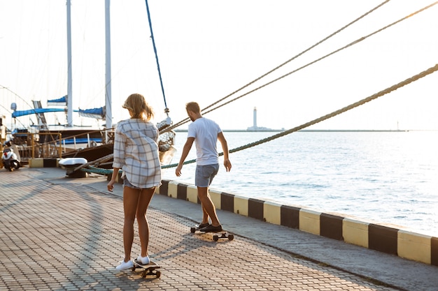 Free photo young beautiful couple walking at seaside, skateboarding.