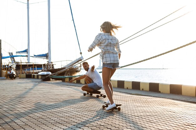 Young beautiful couple walking at seaside, skateboarding.