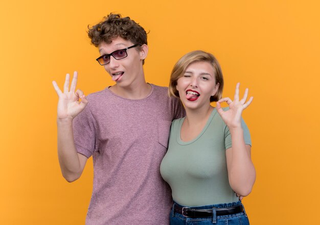 Young beautiful couple wearing casual clothes boy and girl  posing and smiling showing ok sign standing over orange wall