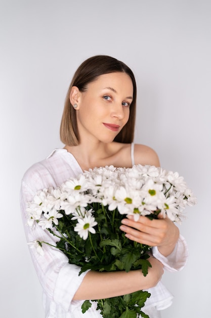 Young beautiful cute sweet lovely smiling woman with hold a bouquet of white fresh flowers on white wall background