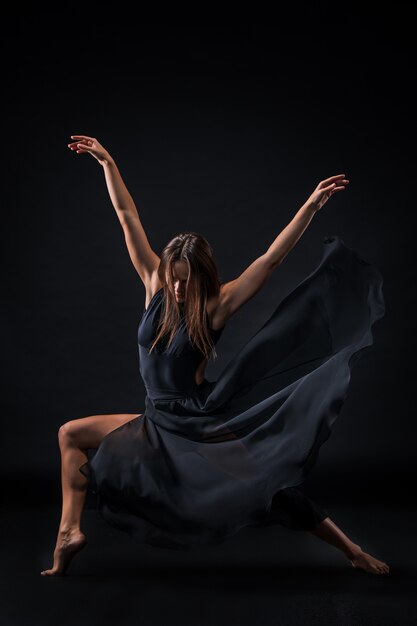 Young beautiful dancer in beige dress dancing on black wall