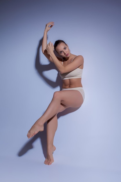 Young beautiful dancer in beige swimwear dancing on lilac studio