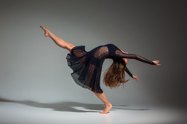 Young beautiful dancer in black dress posing on a dark gray studio background. Modern, Contemporary, improvisation