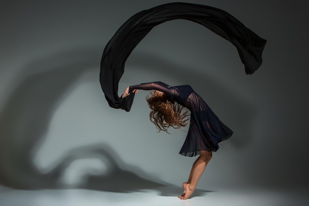 Free Photo young beautiful dancer in black dress posing on a dark gray studio background. modern, contemporary, improvisation