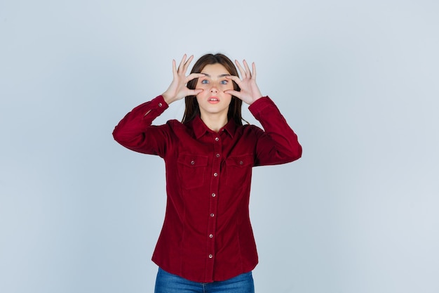 Young beautiful female looking through fingers in shirt and looking focused.