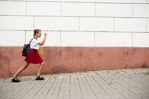 Free Photo young beautiful female student in glasses walking down street, holding folders