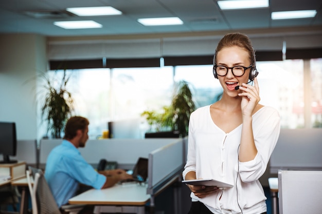 Young beautiful female support phone operator speaking, consulting, over office