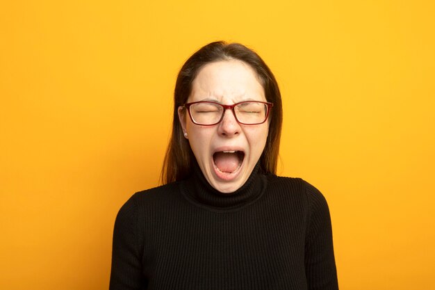 Young beautiful girl in a black turtleneck shouting with annoyed expression 