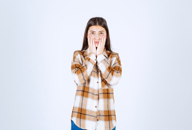 young beautiful girl in casual outfit holding her face on white wall.