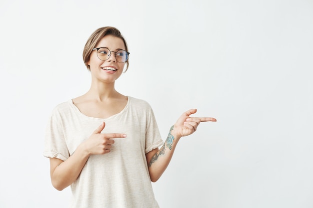 Young beautiful girl in glasses smiling pointing finger in side .