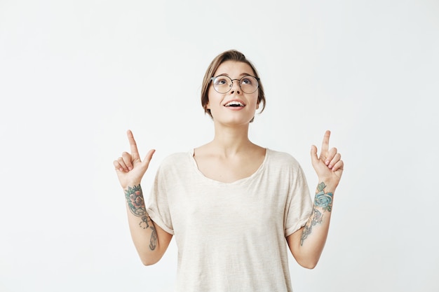 Young beautiful girl in glasses smiling pointing fingers up .