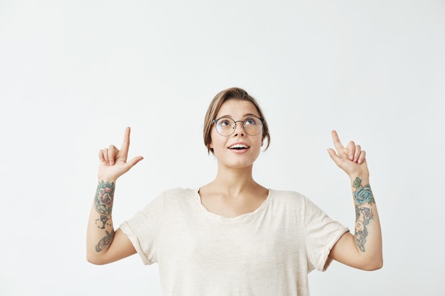 Free photo young beautiful girl in glasses smiling pointing fingers up .