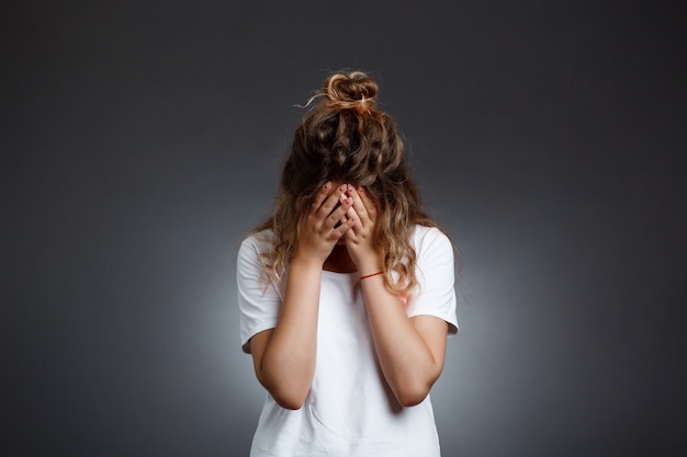 Free photo young beautiful girl hiding face with hands over grey wall.