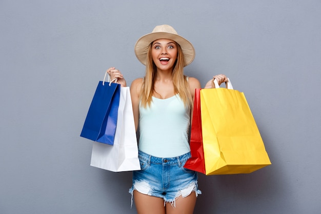 Free photo young beautiful girl holding colorful bags over gray background.