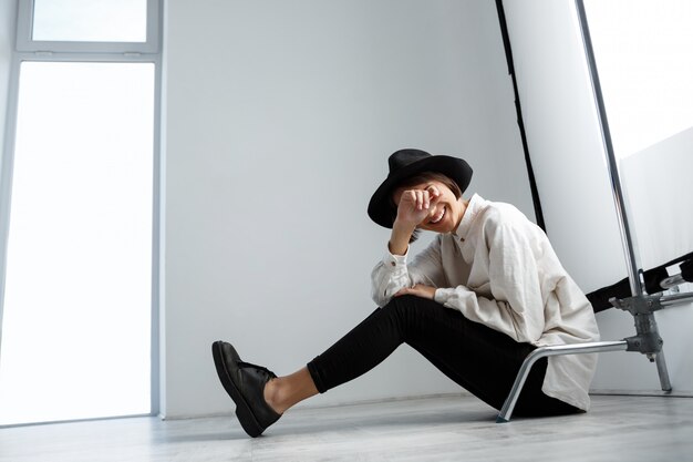 Young beautiful girl laughing sitting on floor over white wall.