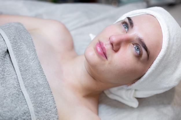 A young beautiful girl lies on the beautician's table and receives procedures, a light facial massage using oil.