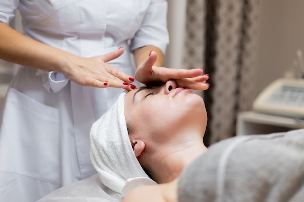 A young beautiful girl lies on the beautician's table and receives procedures, a light facial massage using oil.