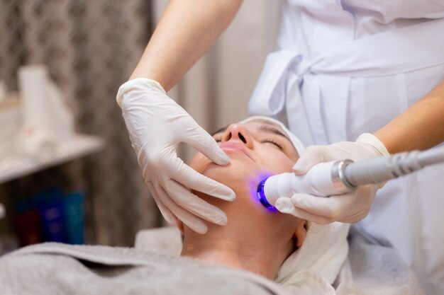 A young beautiful girl lies on the beautician's table and receives procedures with a professional apparatus for skin rejuvenation and moisturizing