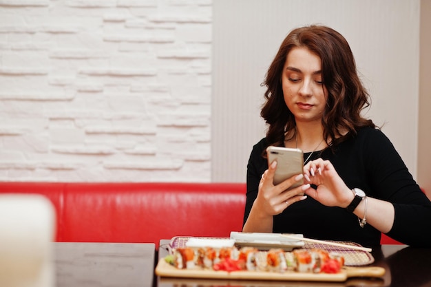 Free photo a young beautiful girl making photo by phone of sushi on traditional japanese restaurant