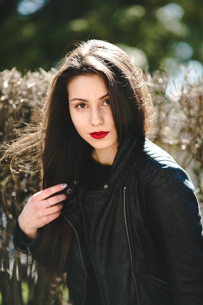 Young beautiful girl posing in a black leather jacket in the park