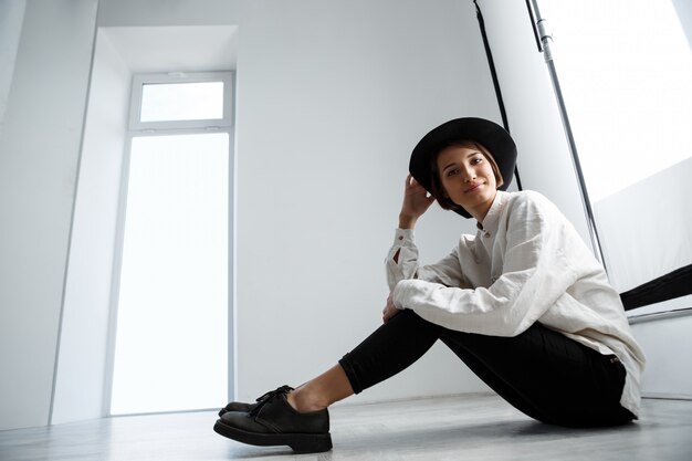 Young beautiful girl smiling sitting on floor over white wall.