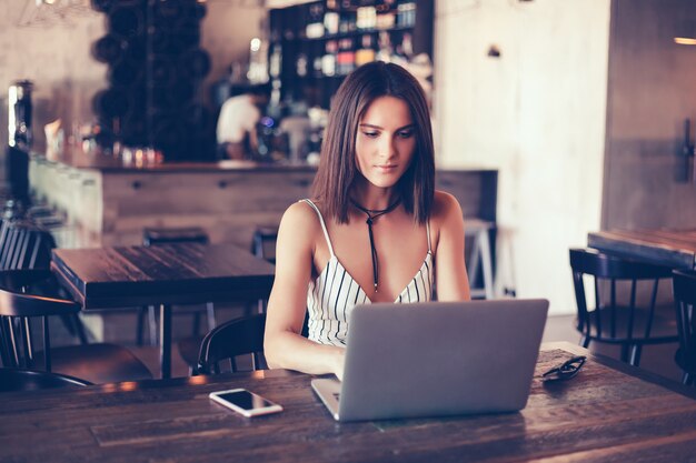 young beautiful girl uses a laptop in cafe, surfing in internet