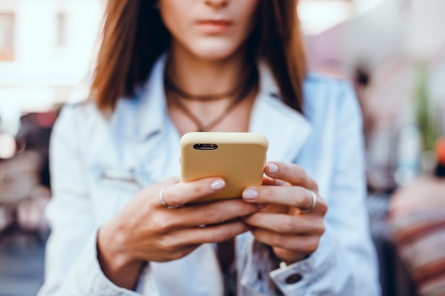 young beautiful girl uses a smartphone on the street, surfing the internet