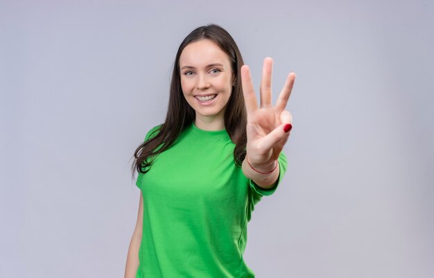 Young beautiful girl wearing green t-shirt smiling cheerfully showing and pointing up with fingers number three standing over isolated white background