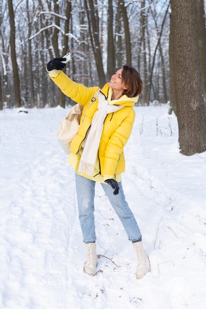 Young beautiful happy cheerful woman in the winter forest video blog, makes a selfie photo