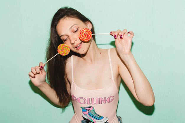 Young beautiful hipster woman posing against blue wall, holding lolly pop candy