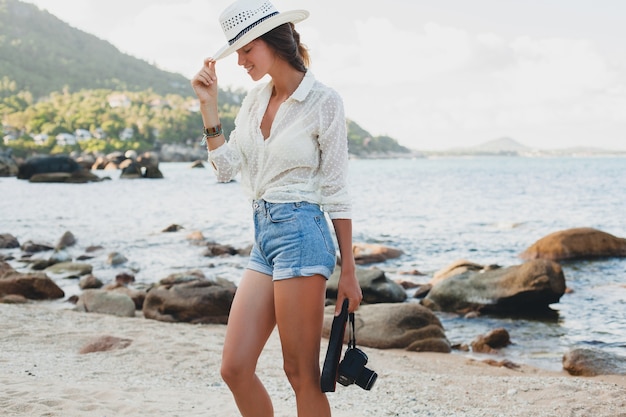 Young beautiful hipster woman on summer vacation in asia, relaxing on tropical beach, digital photo camera, casual boho style, sea landscape , slim tanned body, travel alone