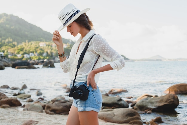 Young beautiful hipster woman on summer vacation in asia, relaxing on tropical beach, digital photo camera, casual boho style, sea landscape , slim tanned body, travel alone